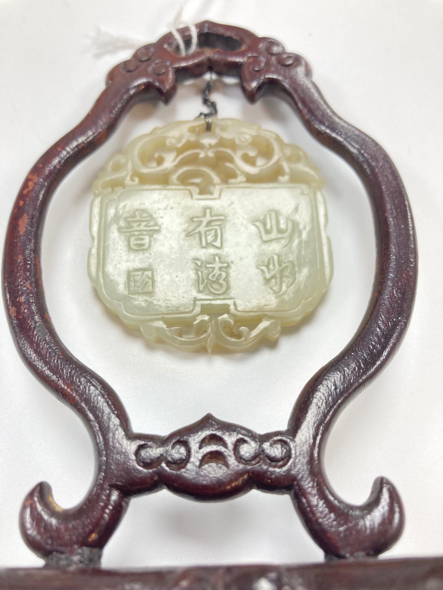 A Chinese pale celadon jade inscribed plaque, 19th/20th century, 5.1cm, suspended from a wood stand